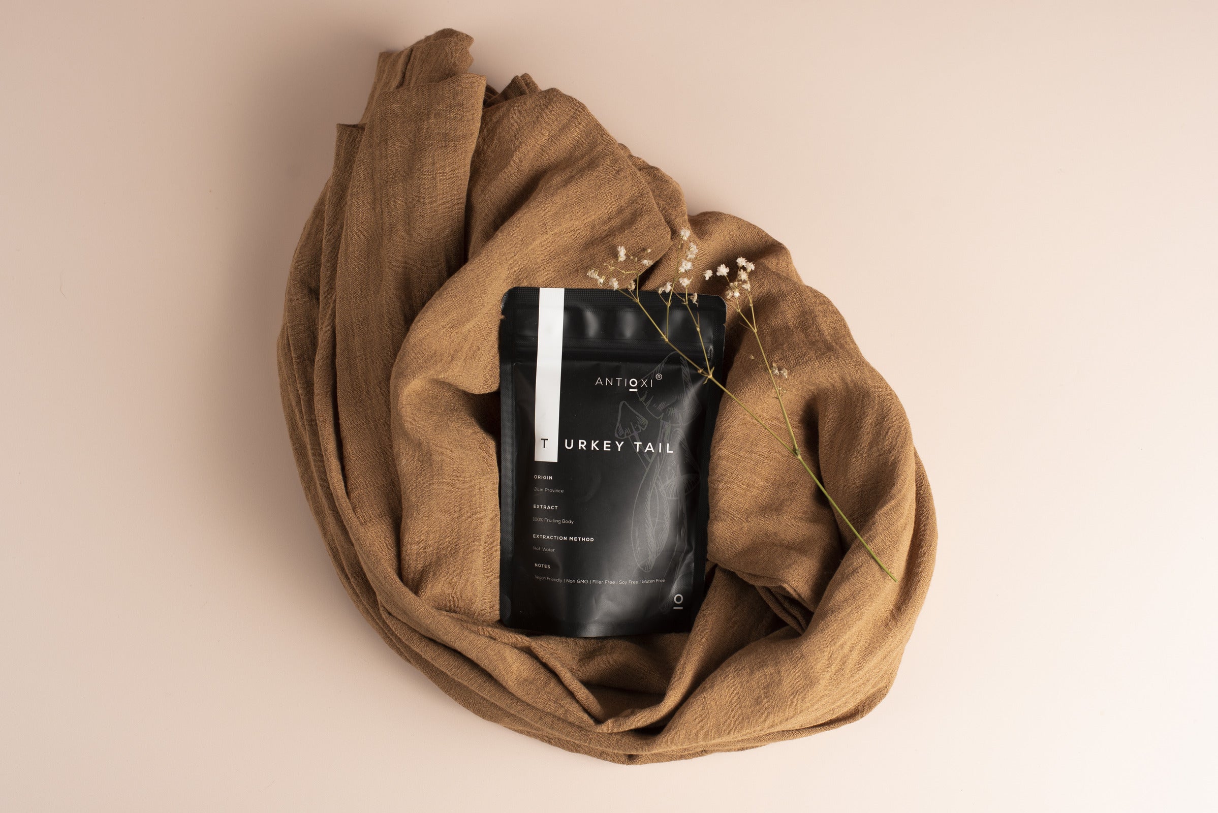 A black pouch of Antioxi Turkey Tail Mushroom supplements wrapped in a brown cloth with a small flower.