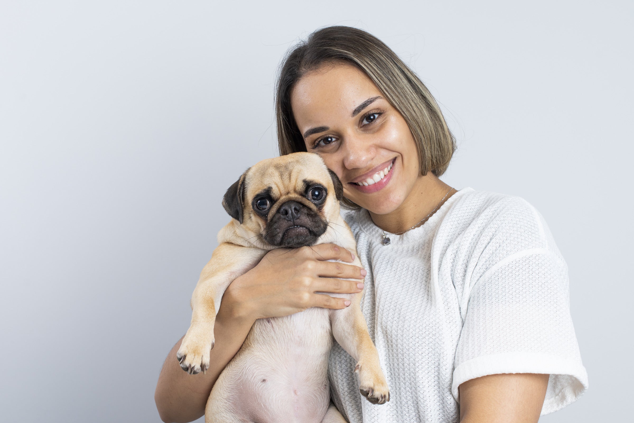 Daniela Vogl, one of Antioxi's founders, is smiling warmly while holding Zalea, a cute pug with light tan fur with a black mask and ears.