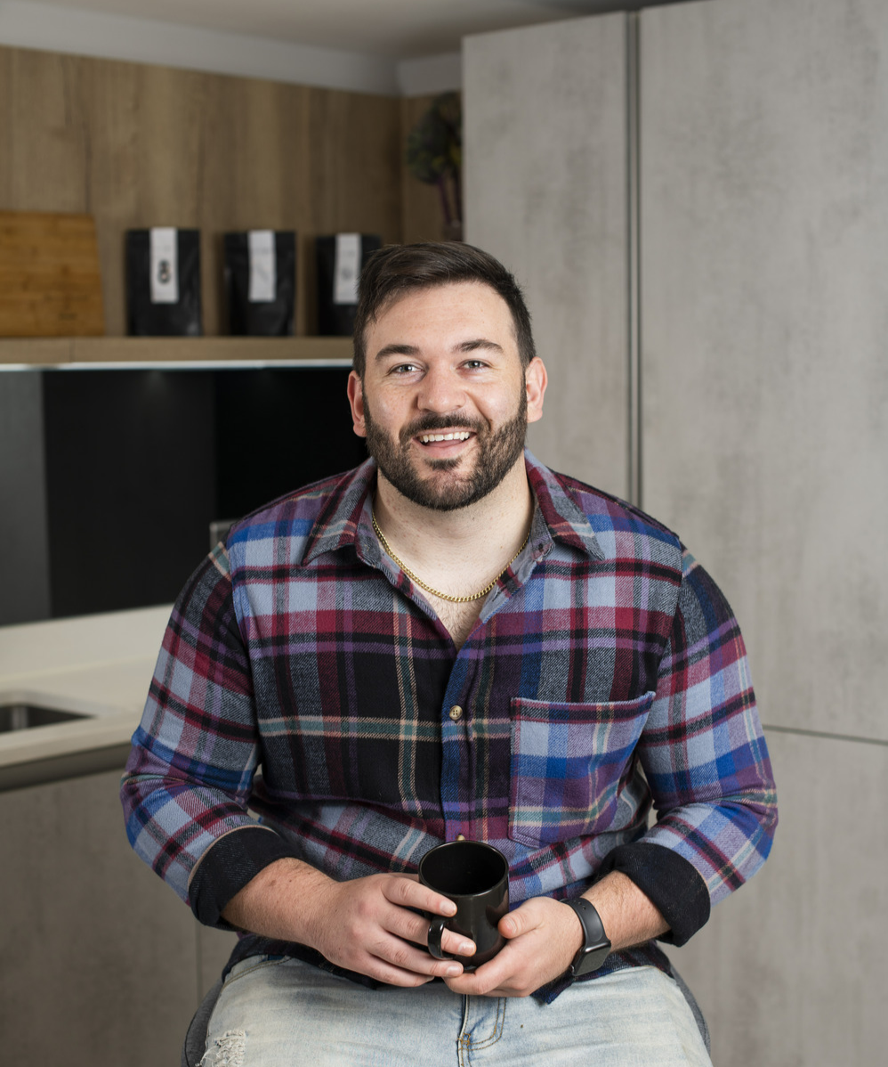 Antioxi Founder Marko Grensemann sitting on a chair in a kitchen, holding a cup of mushroom coffee, with a open and inviting expression.