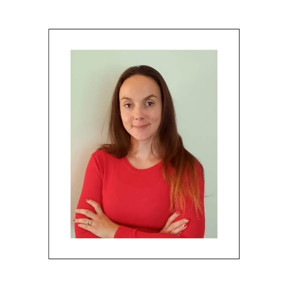 Ramona, dressed in a vibrant red top, stands confidently with her arms crossed, conveying professionalism and dedication.