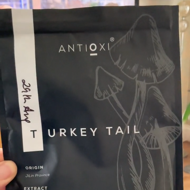 A close-up of a hand holding a pouch of Antioxi Turkey Tail mushroom supplement for pets, showcasing the product's sleek black packaging and origin of the extract.