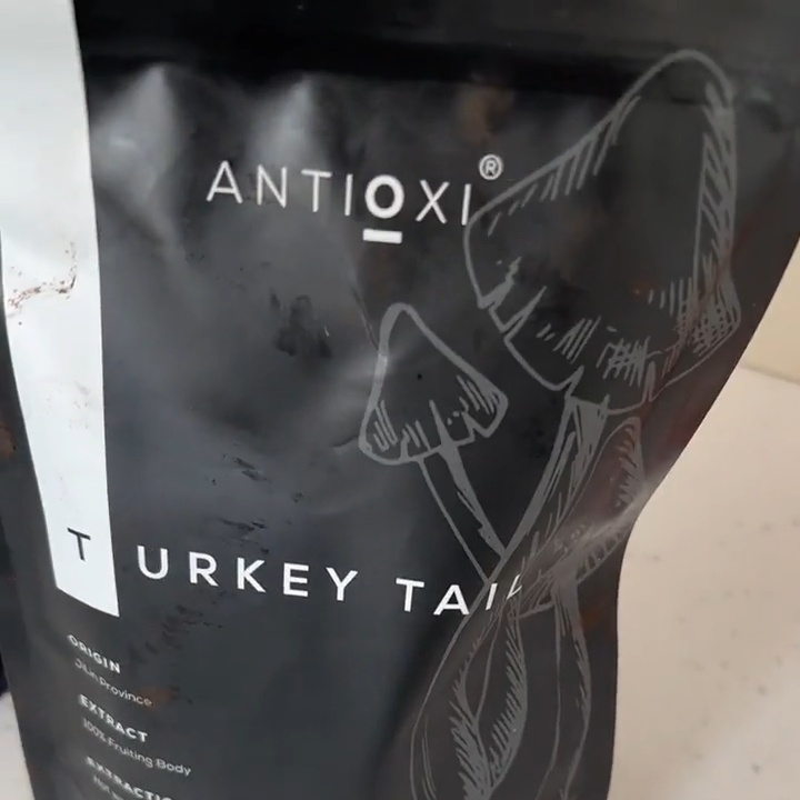 A close-up of a black pouch of Antioxi Turkey Tail mushroom supplements for pets placed on a white surface, emphasizing the product's sleek black packaging and clear labeling with illustrations of a mushrooms.